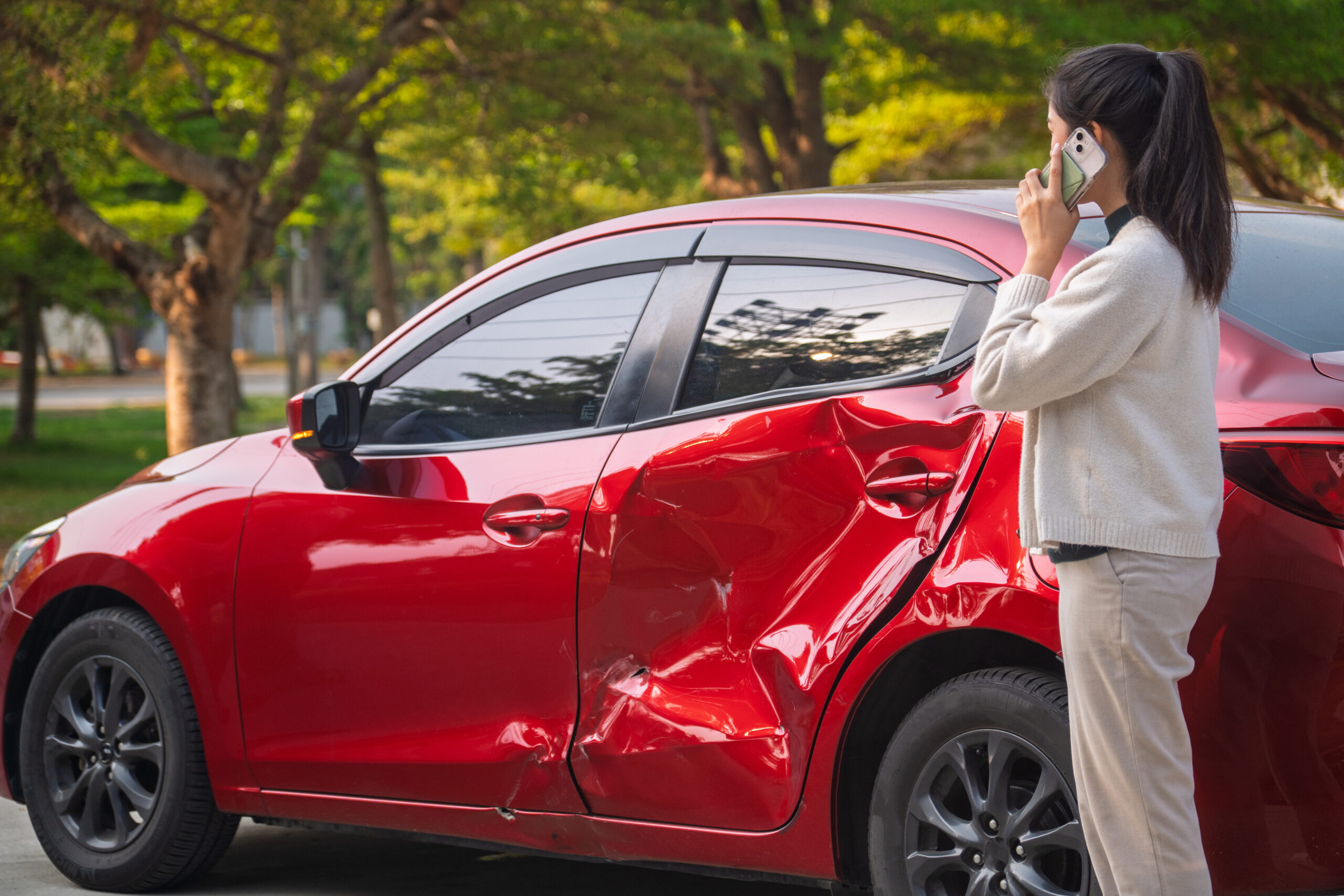A young woman looks at her red sedan that was involved in an accident.