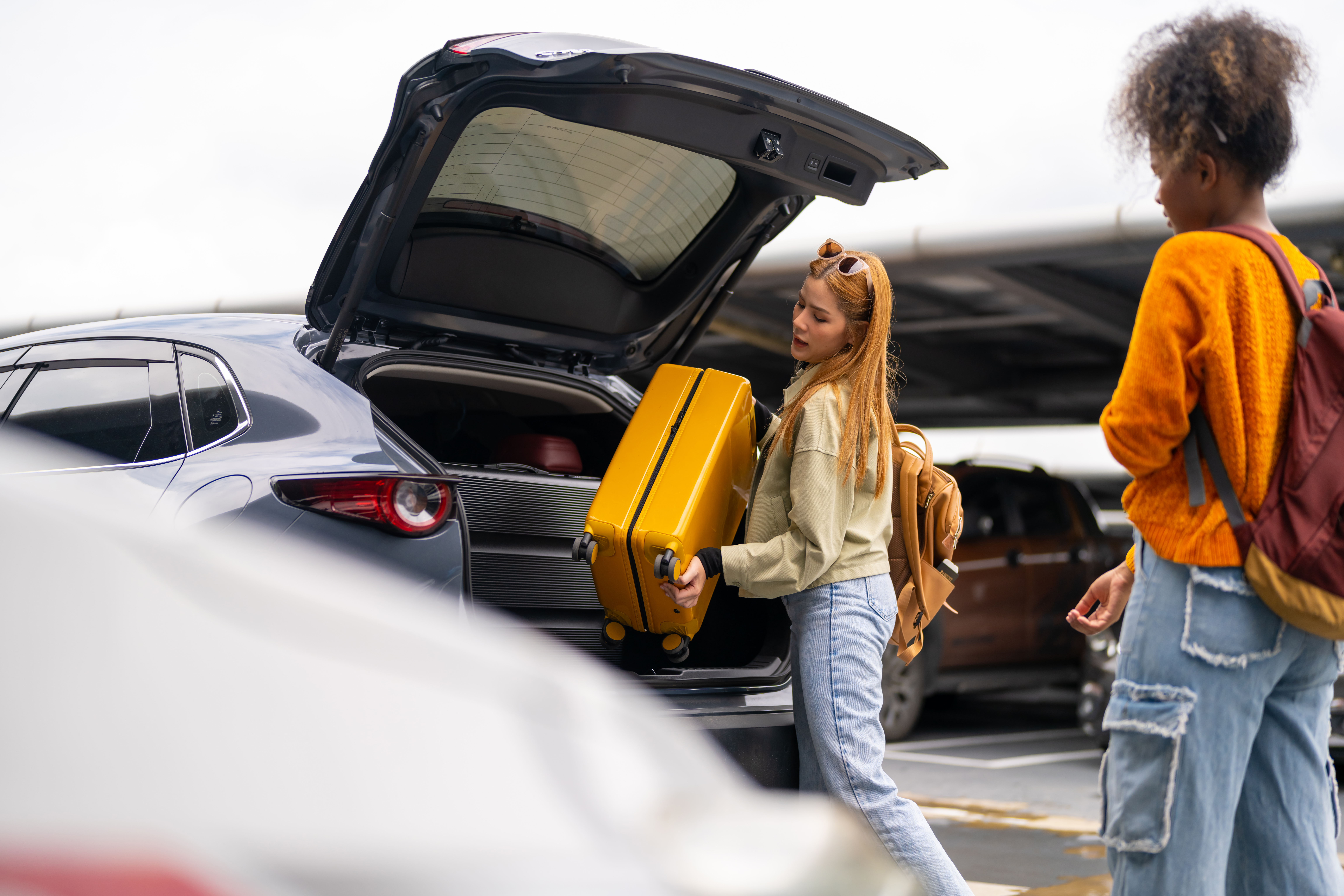 Woman puts luggage into rental car at airport.
