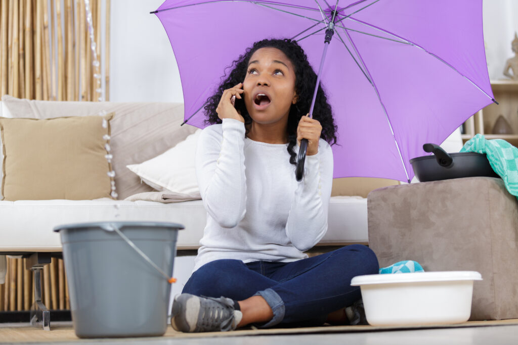Women with umbrella collects water leaking from her ceiling in bucket