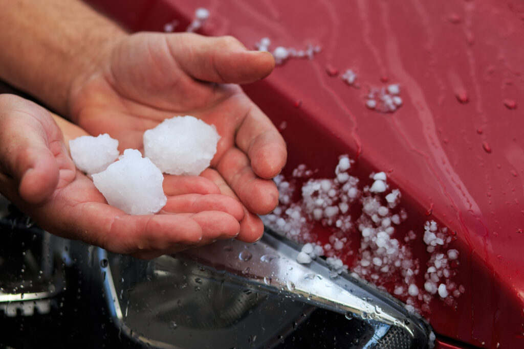 A person holds pieces of hail that impact a car.