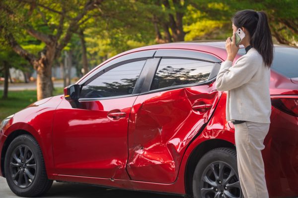 A young woman looks at her red sedan that was involved in an accident.