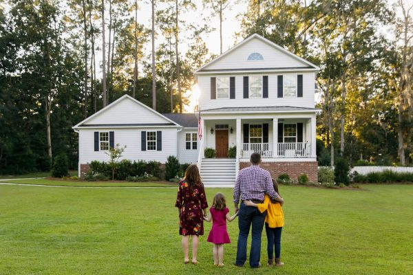 A family of four stands outside their home.
