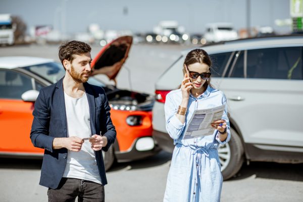 Man and woman arguing, standing together on the road with their cars on the background after the car accident