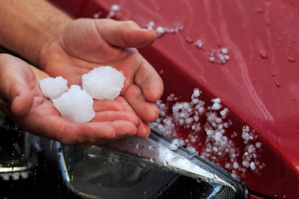 A person holds pieces of hail that impact a car.